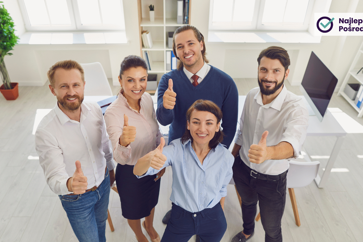 Grupa uśmiechniętych ludzi w biurze podnosi kciuki