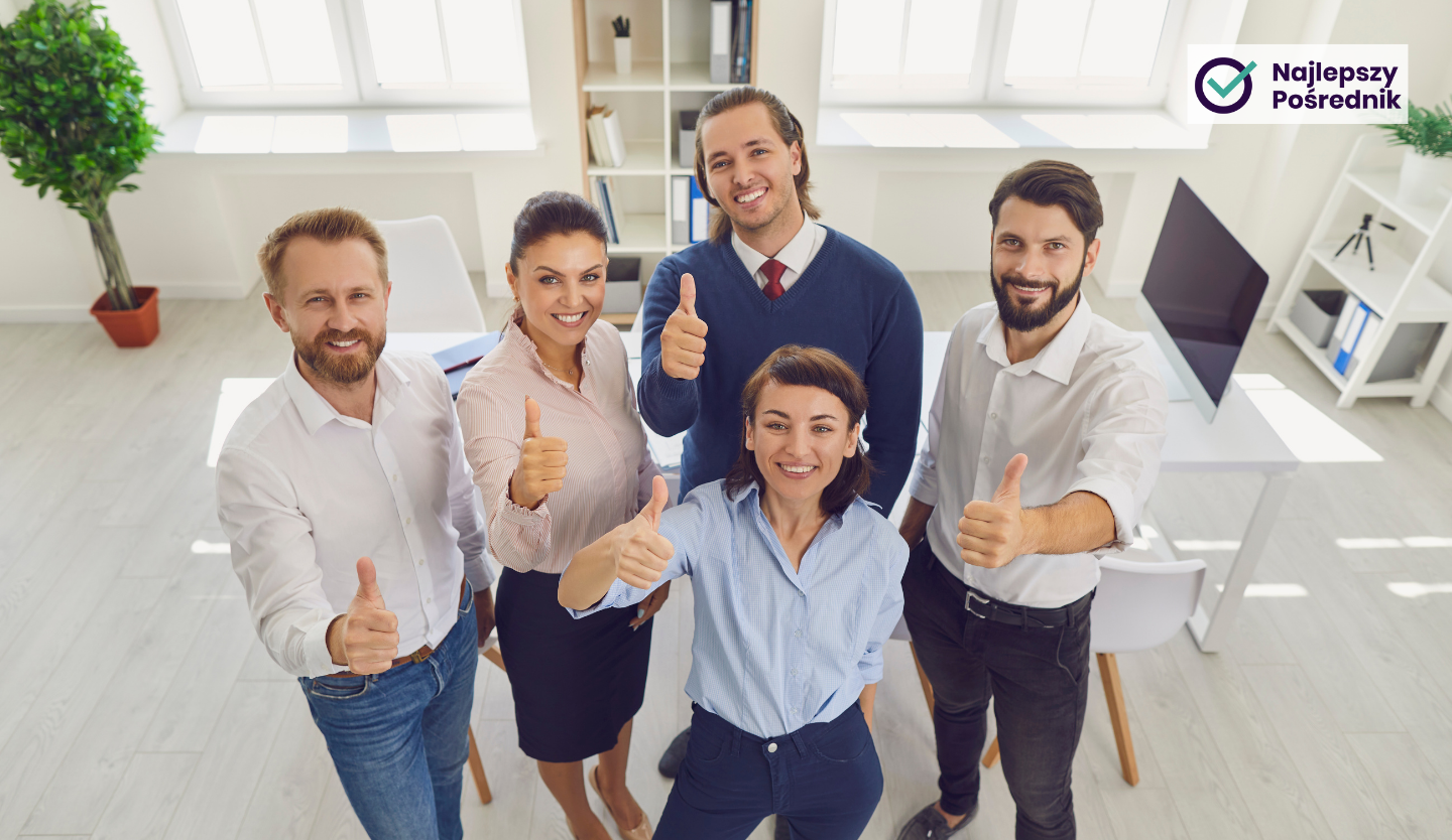 Grupa uśmiechniętych ludzi w biurze podnosi kciuki